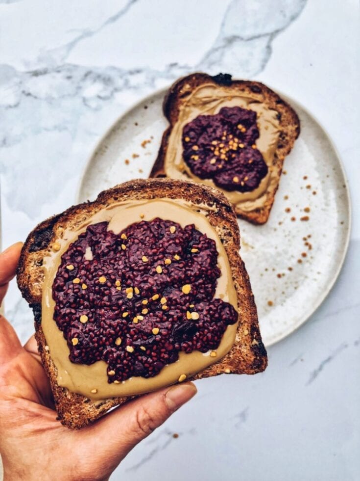 Two pieces of toasts topped with raspberry chia jam and peanut butter.
