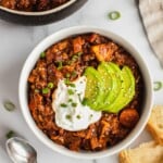 A bowl of sweet potato chili Topped with avocado, yogurt and scallions.