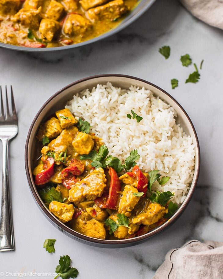 A bowl of jasmine rice and Thai Coconut Curry Chicken. There is a fork on the side.