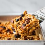 A spatula is serving a piece of freshly baked carrot cake oatmeal bars. This gluten free vegan carrot cake appears to be soft and chewy, perfect for Easter brunch.