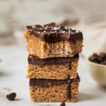 A stack of three peanut butter chocolate bars . The one on top has a bite in it.