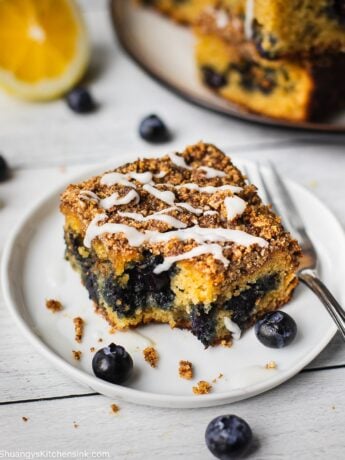 A bite shot is taken from a piece of healthy breakfast dessert. There is a crumbly top and a drizzle of maple coconut butter. There is also blueberries and lemons in the picture