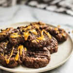 A plate of no bake double chocolate cookies. There are some peanut butter and chocolate chips on top.