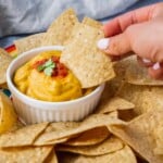 A bowl of creamy vegan queso in the middle of a pile of gluten-free tortilla chips