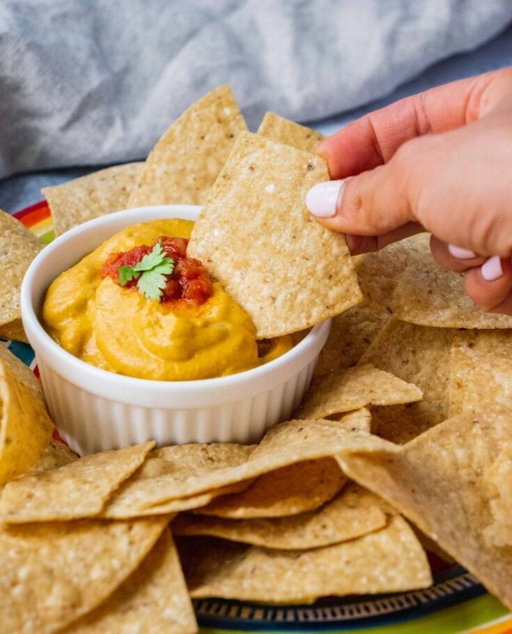 A bowl of creamy vegan queso in the middle of a pile of gluten-free tortilla chips