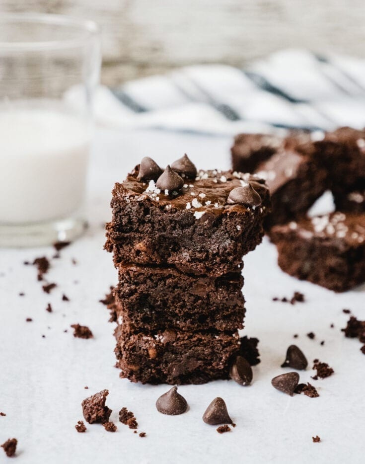 Fudgy Gooey Healthy Brownies stacked up with more brownies and a glass of milk.