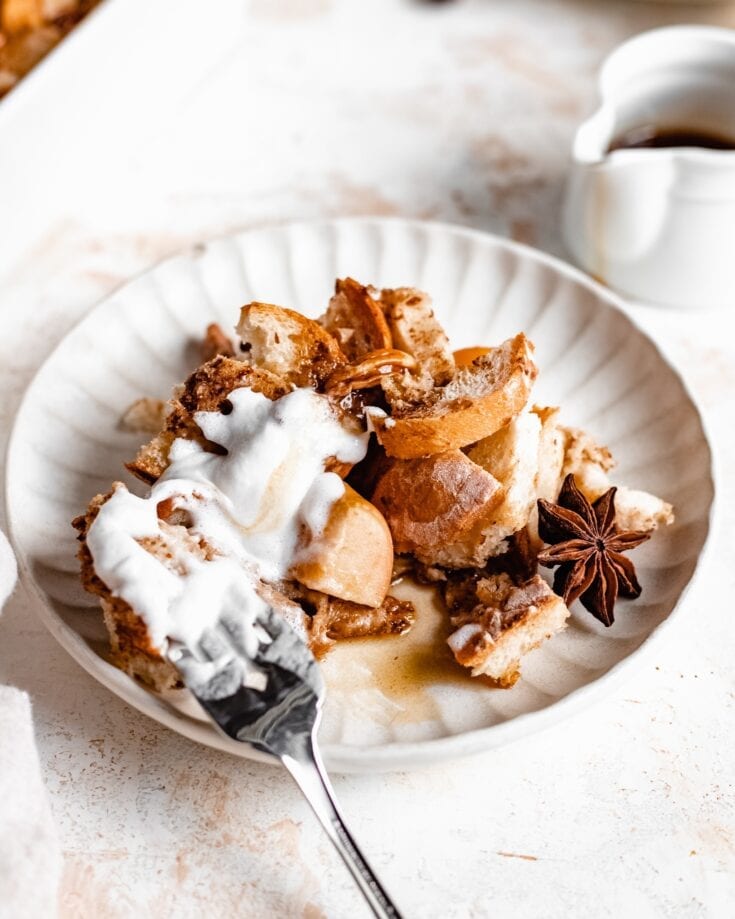 A plate of a apple french toast casserole that is served with coconut cream, candied walnuts and cinnamon apples. This overnight french toast casserole appears to be soft and crunchy.