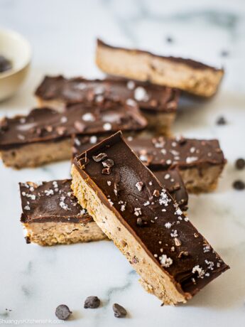 A few pieces of no bake chocolate chip cookie dough bars on the table. There is chocolate layer on top and sea salt sprinkled on it.