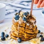 A loaded pancake stack with a cute into it and a fork to grab this thick and fluffy bite.
