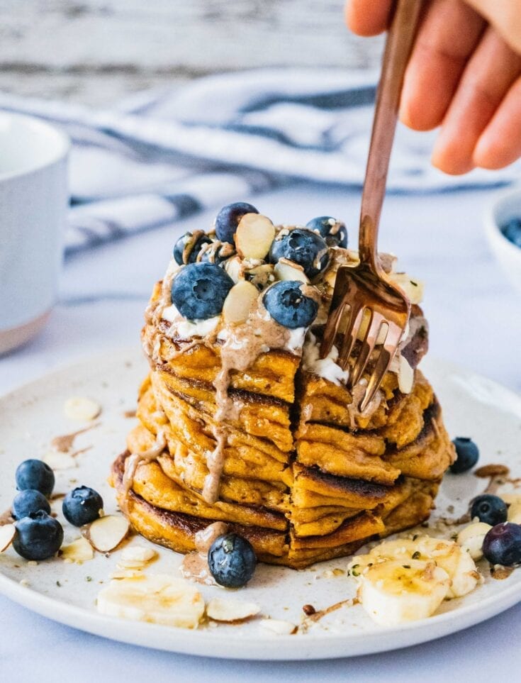 A loaded pancake stack with a cute into it and a fork to grab this thick and fluffy bite.