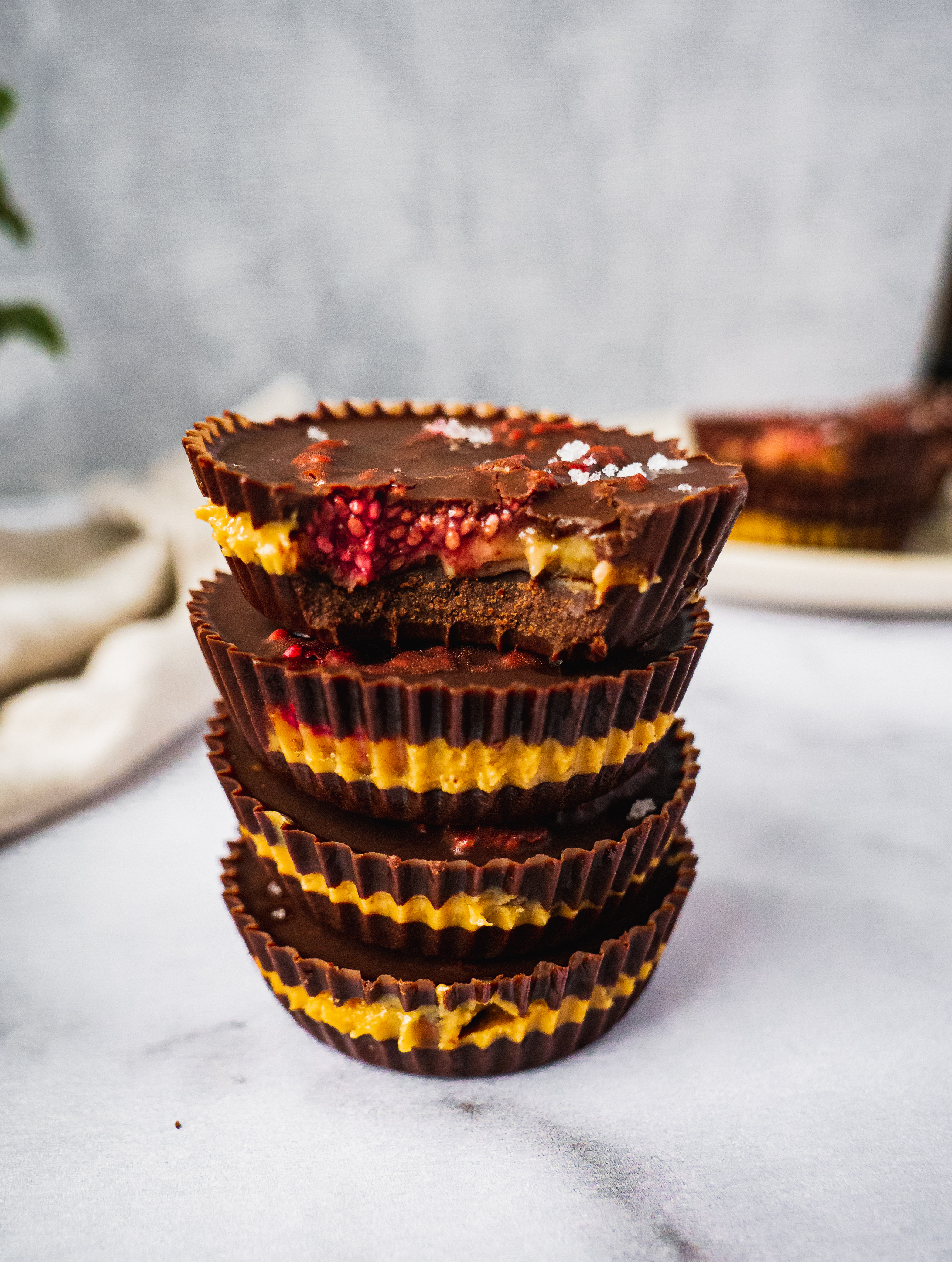 4 peanut butter jelly chocolate cups stack on top of each other. The top cup has a bite. Inside there is the raspberry chia jam and peanut butter banana filling, with sprinkle of sea salt on top.