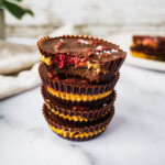 4 peanut butter jelly chocolate cups stack on top of each other. The top cup has a bite. Inside there is the raspberry chia jam and peanut butter banana filling, with sprinkle of sea salt on top.
