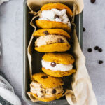 Four Pumpkin Chocolate chip cookie ice cream sandwich in a loaf pan with parchment paper and chocolate chip on the backgroud
