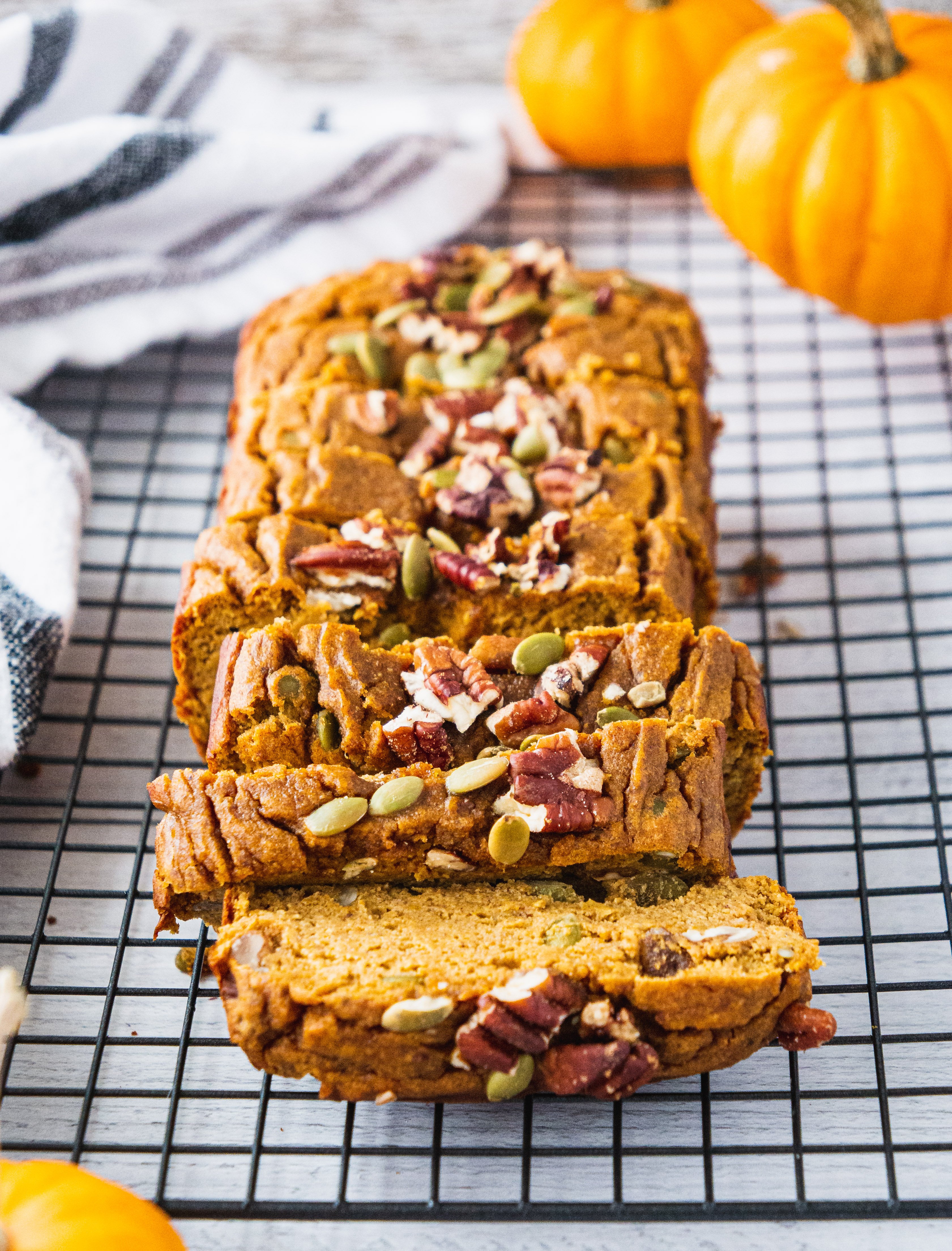 A loaf of sliced up healthy pumpkin bread topped with pumpkin seeds and pecans.