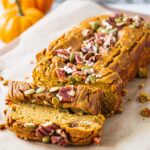 A loaf of sliced up healthy pumpkin bread topped with pumpkin seeds and pecans.