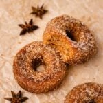 Three baked gluten-free apple cider donuts coated with cinnamon sugar