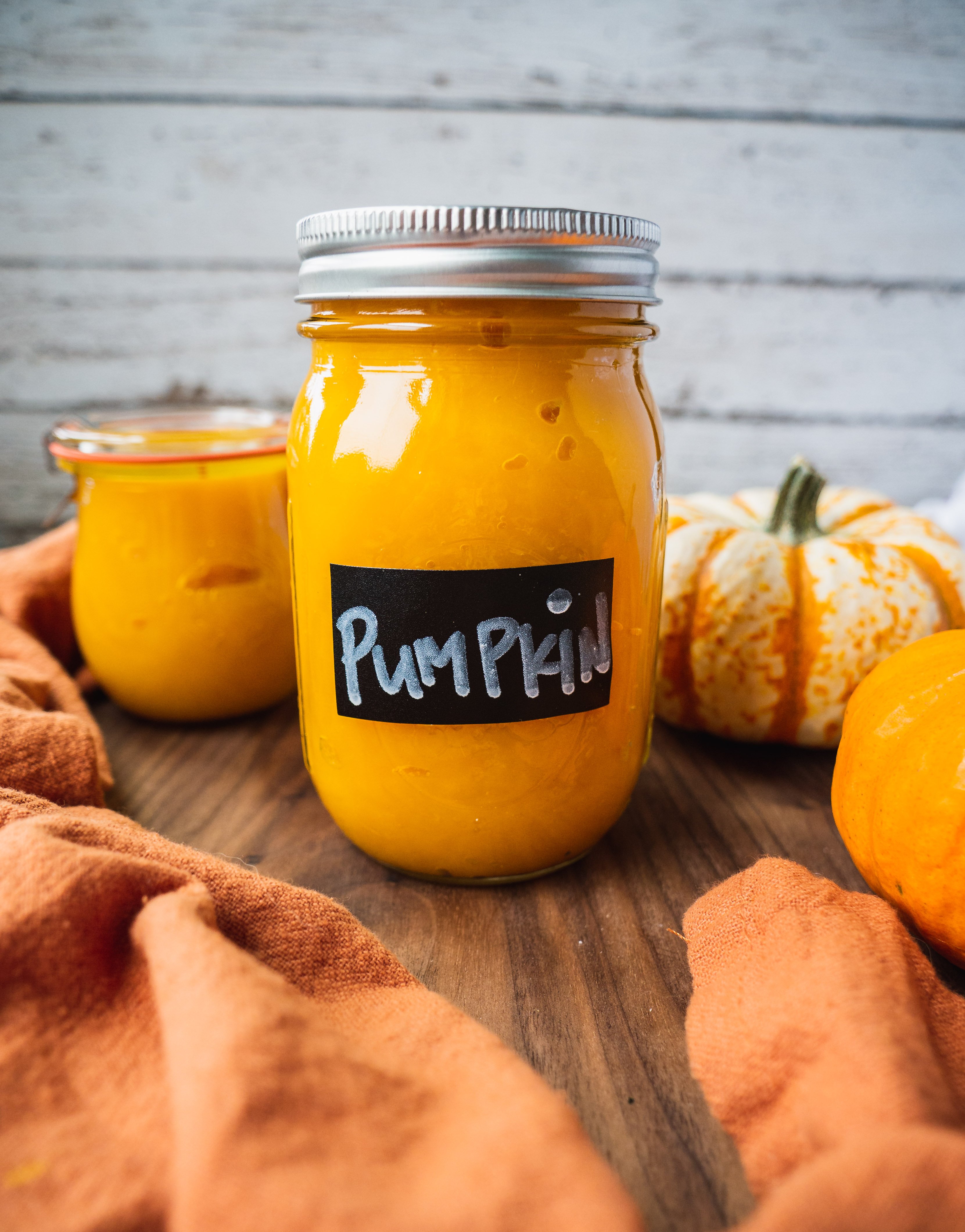 a jar of fresh pumpkin puree homemade from scrach. There is a pumpkin in the background.