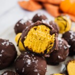 A piece of pumpkin spice chocolate truffle with a bite in the middle. There is a orange kitchen towel in the background.