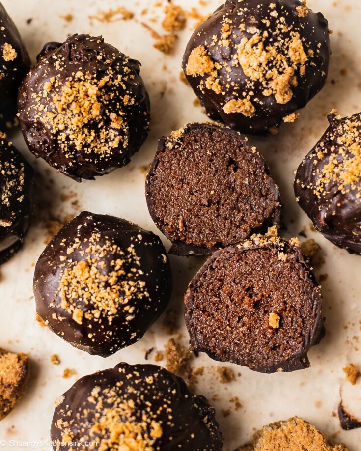 A batch of vegan chocolate truffles that is gingerbread flavored, topped with gingersnap cookies. One of the chocolate truffle is cut in half and the texture is gooey and smooth.