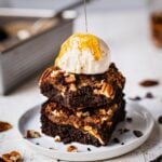 A stack of pecan pie brownies topped with dairy free vanilla ice cream on top of the pecan pie filling and paleo brownie.