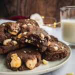 A Plate of White Chocolate Macadamia Nut cookies with a glass of milk in the background. One of them has a bite in it.