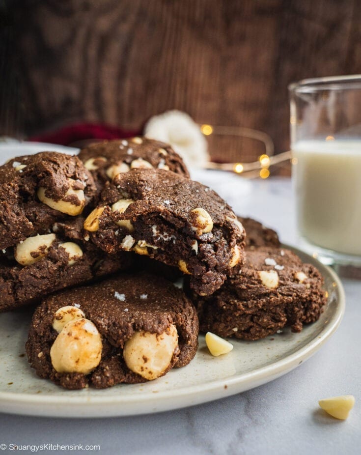 A Plate of White Chocolate Macadamia Nut cookies with a glass of milk in the background. One of them has a bite in it.