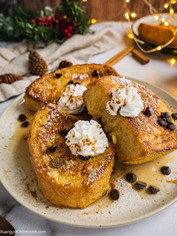 A plate of dairy free eggnog french toast topped with dairy free whip cream and chocolate chips. There is Christmas decoration in the background.
