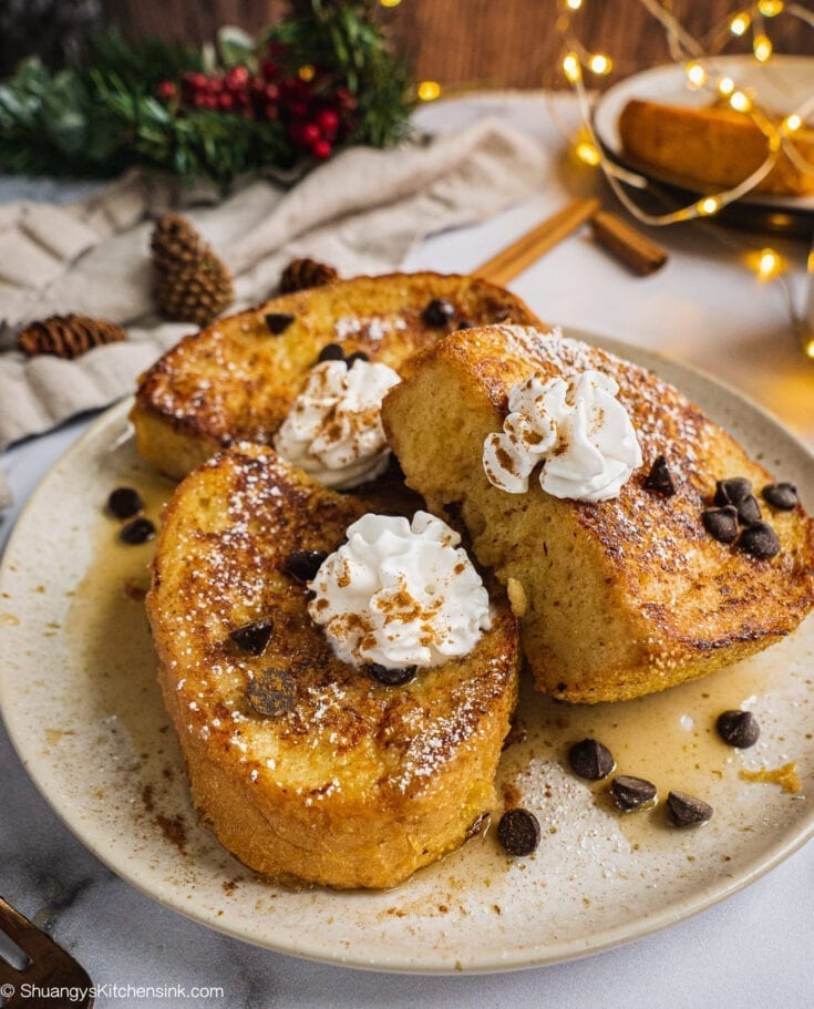 A plate of dairy free eggnog french toast topped with dairy free whip cream and chocolate chips. There is Christmas decoration in the background.