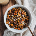 A bowl of paleo, vegan and low sugar gingerbread granola with a glass of milk in the bakcground.