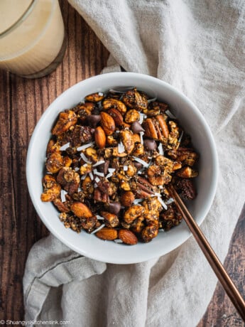 A bowl of paleo, vegan and low sugar gingerbread granola with a glass of milk in the bakcground.