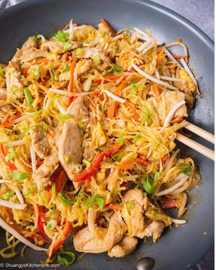 A pan of Pad thai noodles made with spaghetti Squash. There are a pair of chopsticks on the side of the pan.