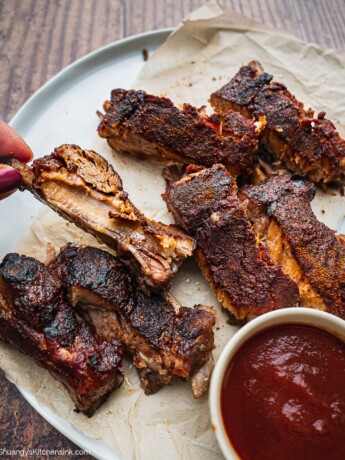 Charred Slow Cooker Whole30 BBQ Ribs on a piece of parchment paper. There is a jar of BBQ Sauce on the side.