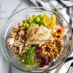 A bowl of classic chicken salad with celery, apples, cranberries, walnuts and dill on top.