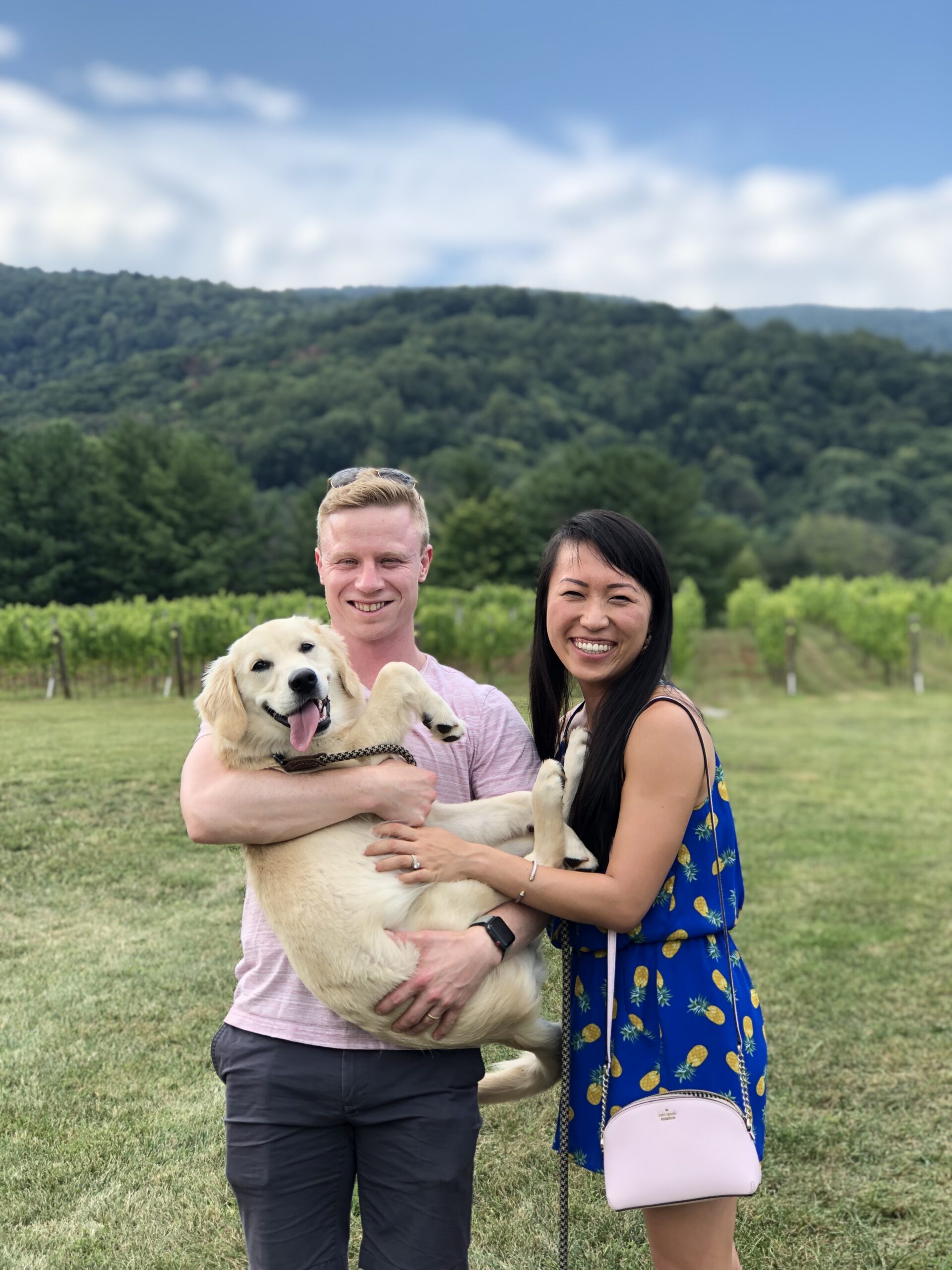 Tom and Shuang holding their Golden Retriever Muffin in front of a mountain