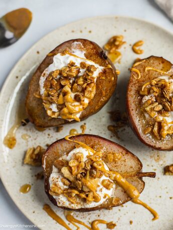 A plate of whole baked pears stuffed with vegan yogurt, granola, honey and walnuts and nut butter. Oven baked pears are spiced with cinnamon.