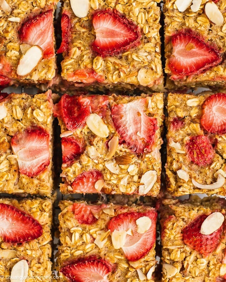 Freshly baked and cut strawberry oatmeal bake on a cooling wrap. There are fresh strawberry and sliced almonds on top.