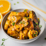 A bowl fo whole30 orange chicken ready to be served. The healthy orange chicken is juicy and tender, coated with tangy orange sauce. There is a pair of chopsticks.