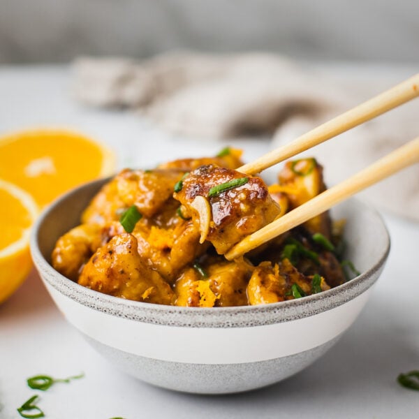 A bowl of orange chicken with chopsticks