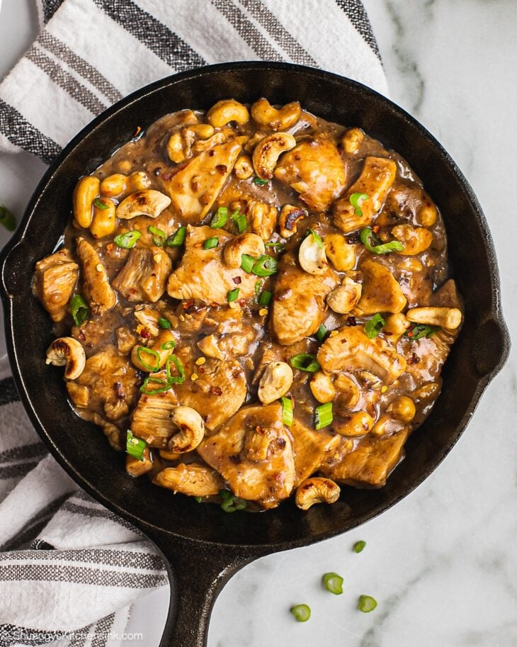A pan of cashew chicken topped with crunchy cashews and fresh scallions