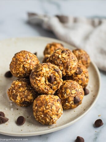 A plate of peanut butter oatmeal balls. There is a bite on the top one. There are a few chocolate chips on the plate and table.