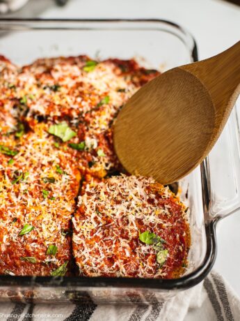 Freshly Bake Eggplant Parmesan just came out of the oven. There is a spoon holding up one piece.