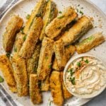 A plate of zucchini fries on a plate. There is a serving dish with garlic aioli.