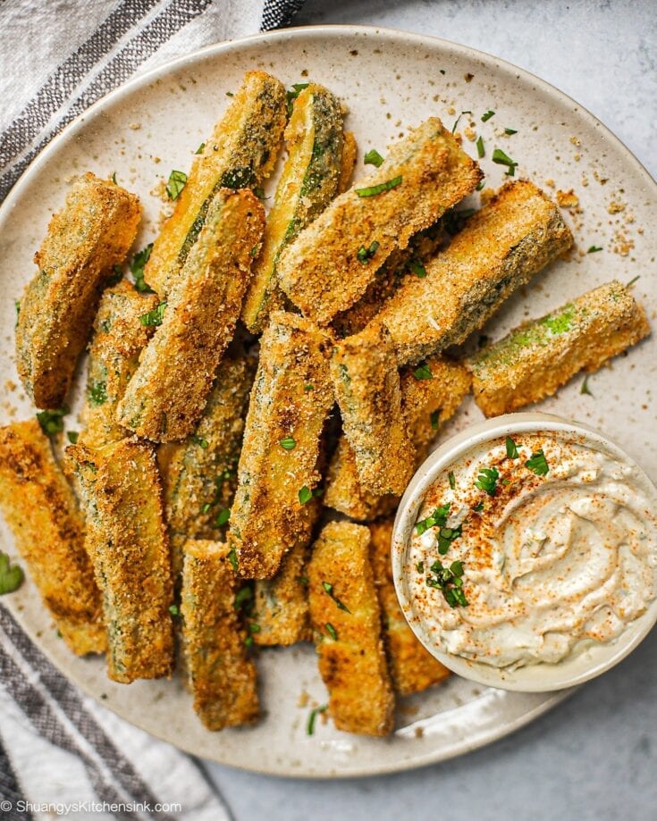 A plate of zucchini fries on a plate. There is a serving dish with garlic aioli.