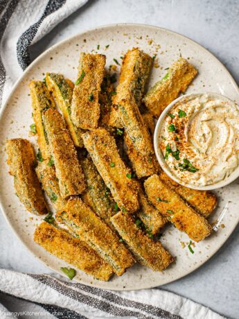 A plate of zucchini fries on a plate. There is a serving dish with garlic aioli.