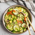 A bowl of asian cucumber salad. There are cucumbers, red bell pepper, red onion and black sesame seeds.