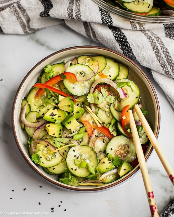 A bowl of asian cucumber salad. There are cucumbers, red bell pepper, red onion and black sesame seeds.