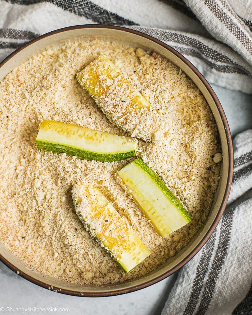 zucchini being coated with bread crumbs 