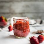 A jar of strawberry chia jam. There are a few strawberries on the side.