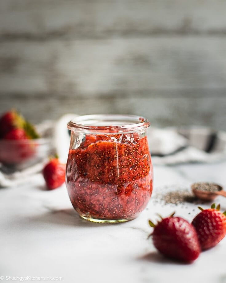 A jar of strawberry chia jam. There are a few strawberries on the side.