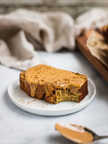 A slice of zucchini banana bread on the table. There is almond butter and cinnamon on top. There is a bite.